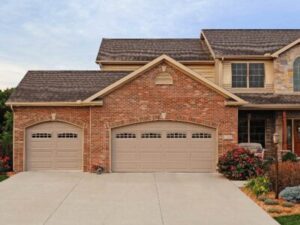 Two-story split-level home with stone and brick facade and two tan garage doors, one double, the other single, both with arched tops